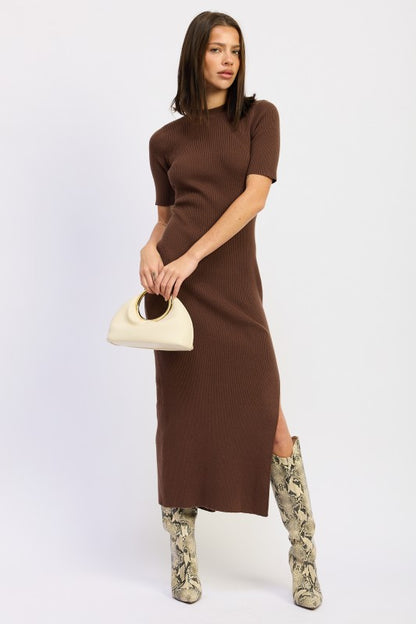 Woman wearing a ribbed knit sweater dress with side slit, styled with knee-high boots and minimalist accessories.