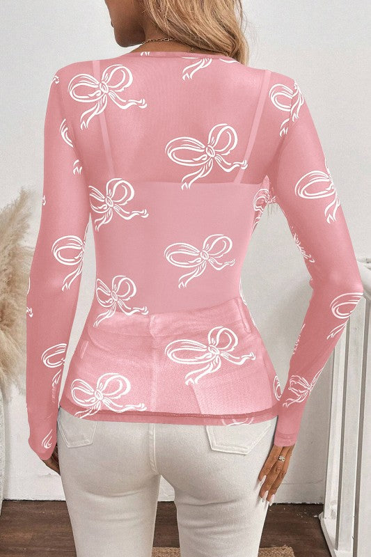 Pink long-sleeve top with white bow pattern worn by a person indoors.