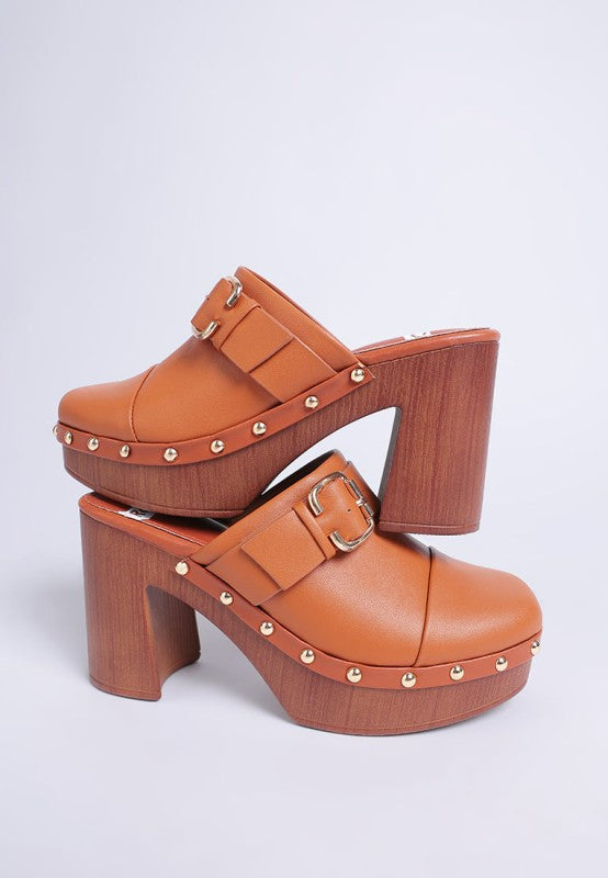 Pair of brown platform clogs with gold studs on a light gray background