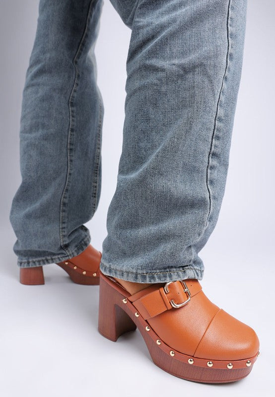 Brown clogs with wooden soles worn with blue jeans on a white background