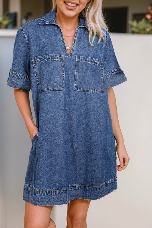 a woman wearing a denim mini dress. The dress has short sleeves, a collared neckline, and pockets.