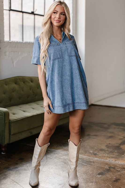 a woman wearing a denim mini dress. The dress has short sleeves, a collared neckline, and pockets.