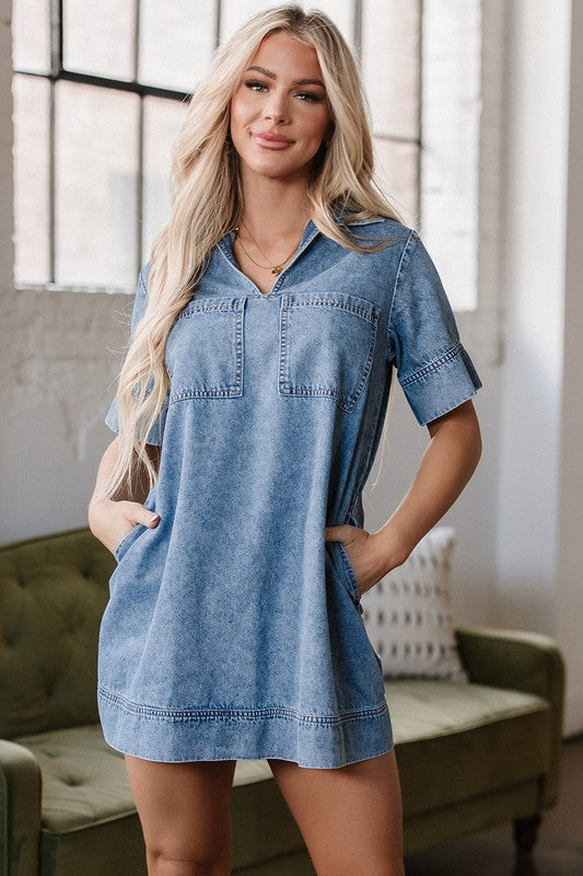 a woman wearing a denim mini dress. The dress has short sleeves, a collared neckline, and pockets.