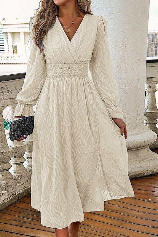 Woman wearing a cream long sleeve midi dress with a smocked waist and flowing skirt, styled with a clutch on a balcony setting.