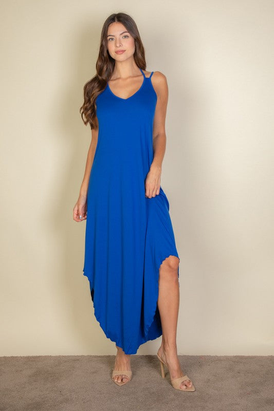 A woman with long brown hair is posing in a royal blue, sleeveless midi dress with a V-neck and a slit on one side. She's wearing tan heels and standing on a beige carpet against a beige wall.
