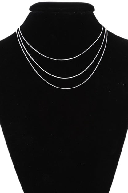Layered gold necklace set displayed on black velvet, featuring three minimalist chains of varying lengths, perfect for a sleek, modern look.