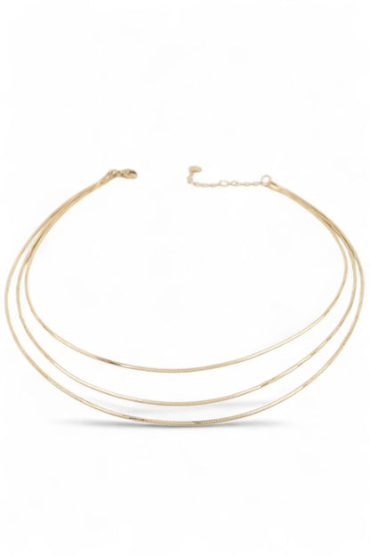 Layered gold necklace set displayed on black velvet, featuring three minimalist chains of varying lengths, perfect for a sleek, modern look.