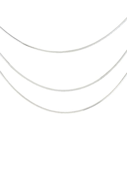 Layered gold necklace set displayed on black velvet, featuring three minimalist chains of varying lengths, perfect for a sleek, modern look.
