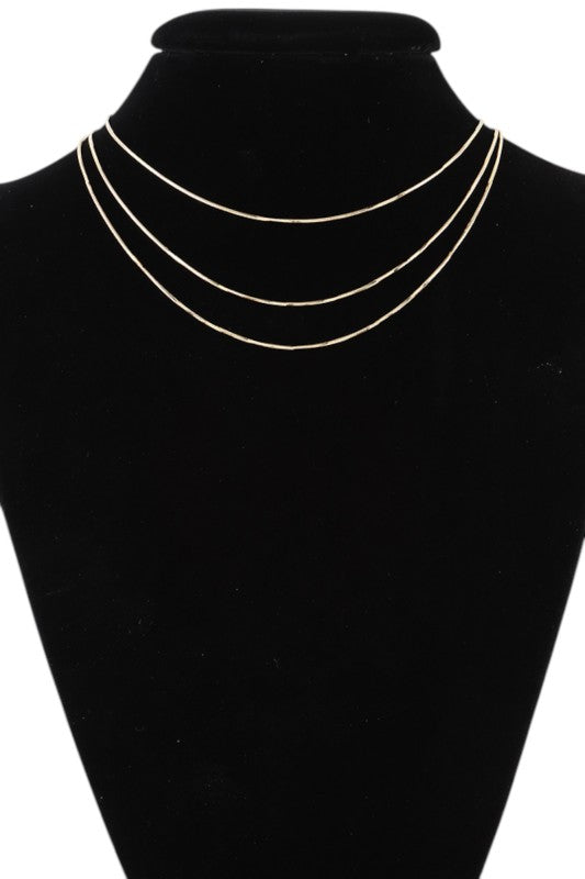 Layered gold necklace set displayed on black velvet, featuring three minimalist chains of varying lengths, perfect for a sleek, modern look.