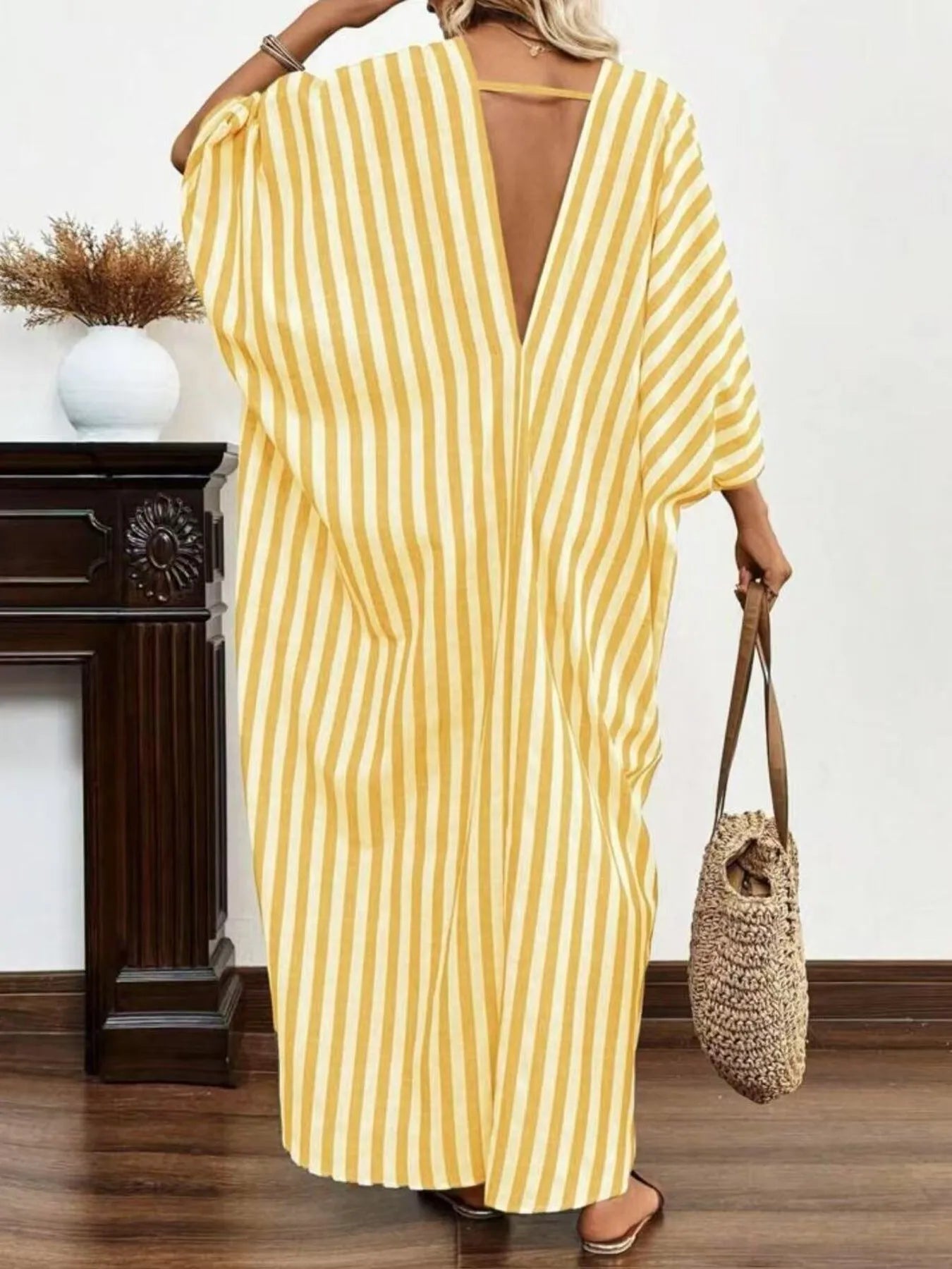 A woman rocking a yellow and white striped maxi dress with a V-neck and loose sleeves.