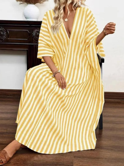 A woman rocking a yellow and white striped maxi dress with a V-neck and loose sleeves.