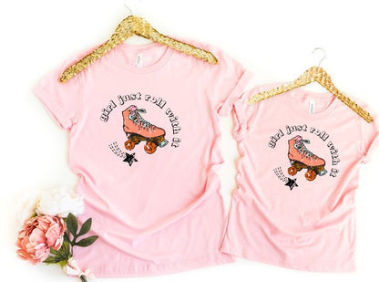 Two pink t-shirts with a roller skate graphic and text on hangers with gold trim.