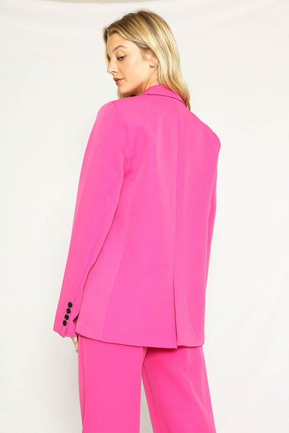 A woman rocking a hot pink suit with a blazer and matching pants. She's got long blonde hair and the suit has black buttons.