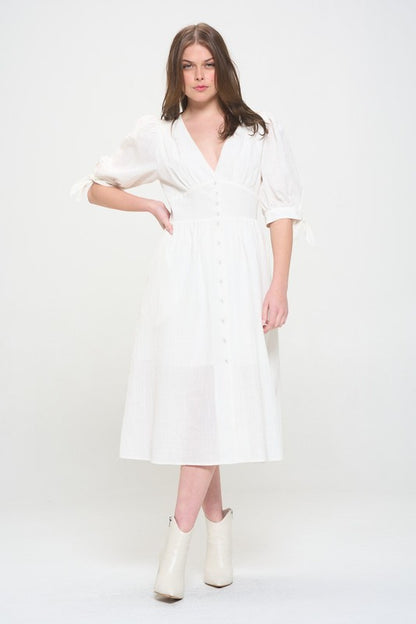 Woman wearing a white textured button-down midi dress with ¾ puff sleeves and tie detail.