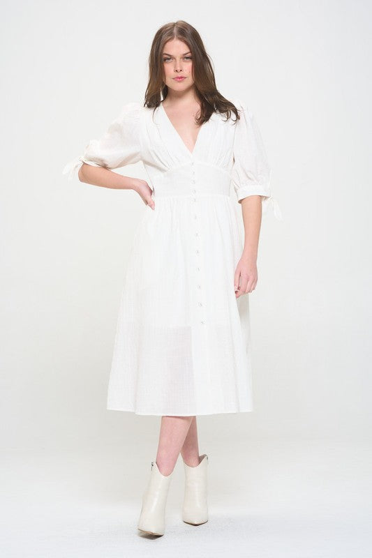Woman wearing a white textured button-down midi dress with ¾ puff sleeves and tie detail.