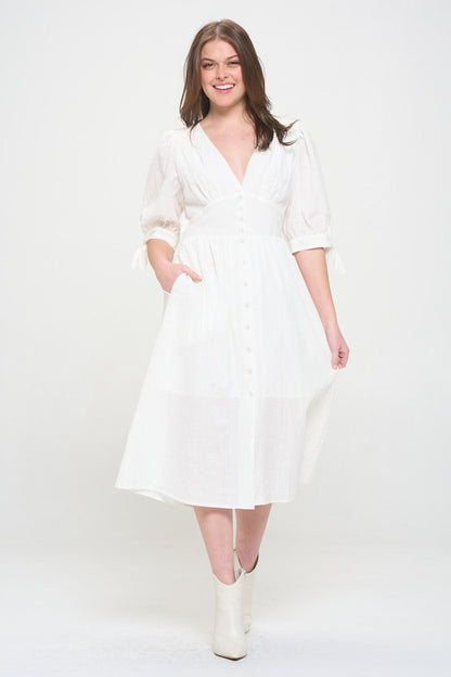 Woman wearing a white textured button-down midi dress with ¾ puff sleeves and tie detail.