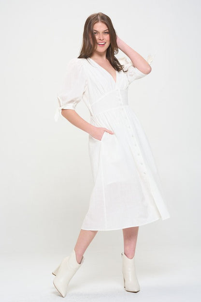 Woman wearing a white textured button-down midi dress with ¾ puff sleeves and tie detail.