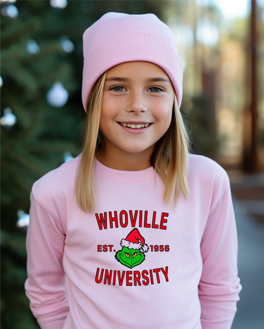 Child wearing a pink 'Whoville University' shirt with a Christmas tree in the background