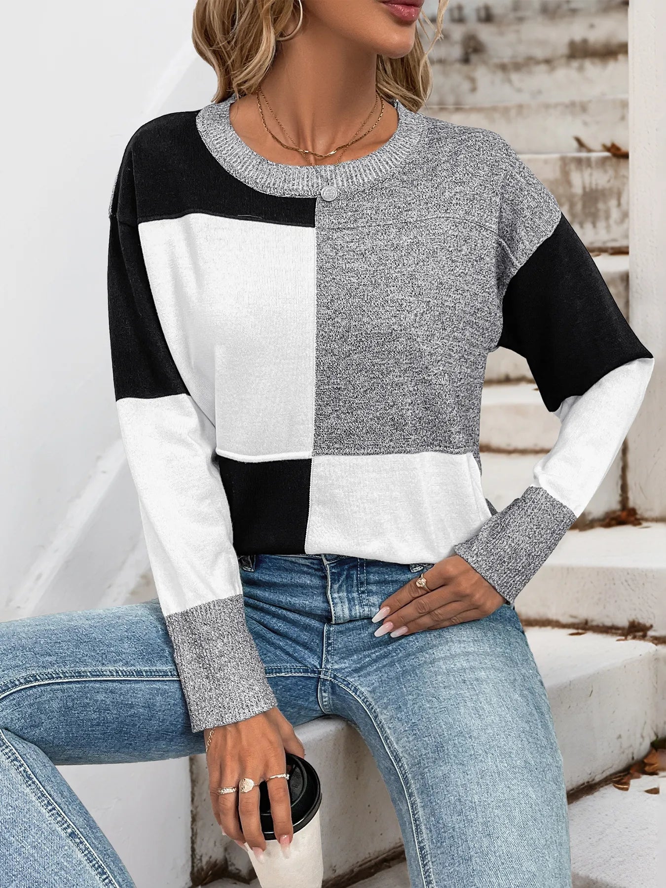Woman wearing a black and white color block sweater with gray speckled sleeves and a crew neck, front view.