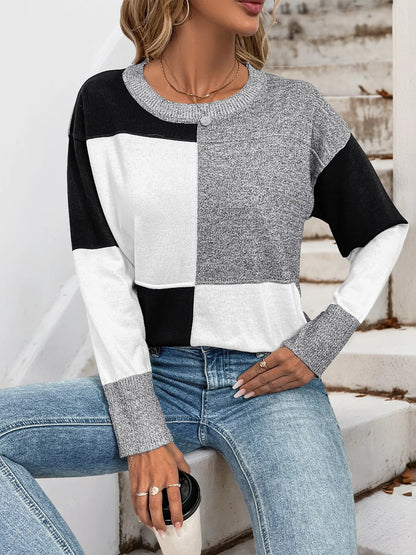 Woman wearing a black and white color block sweater with gray speckled sleeves and a crew neck, front view.