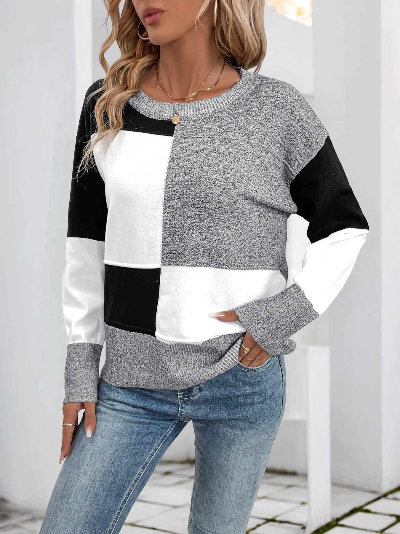 Woman wearing a black and white color block sweater with gray speckled sleeves and a crew neck, posing with hands in pocket.