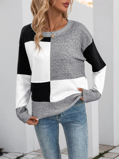 Woman wearing a black and white color block sweater with gray speckled sleeves and a crew neck, semi full length view.