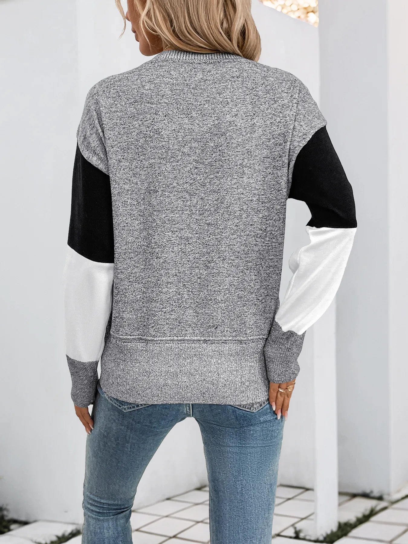 Woman wearing a black and white color block sweater with gray speckled sleeves and a crew neck, back view.