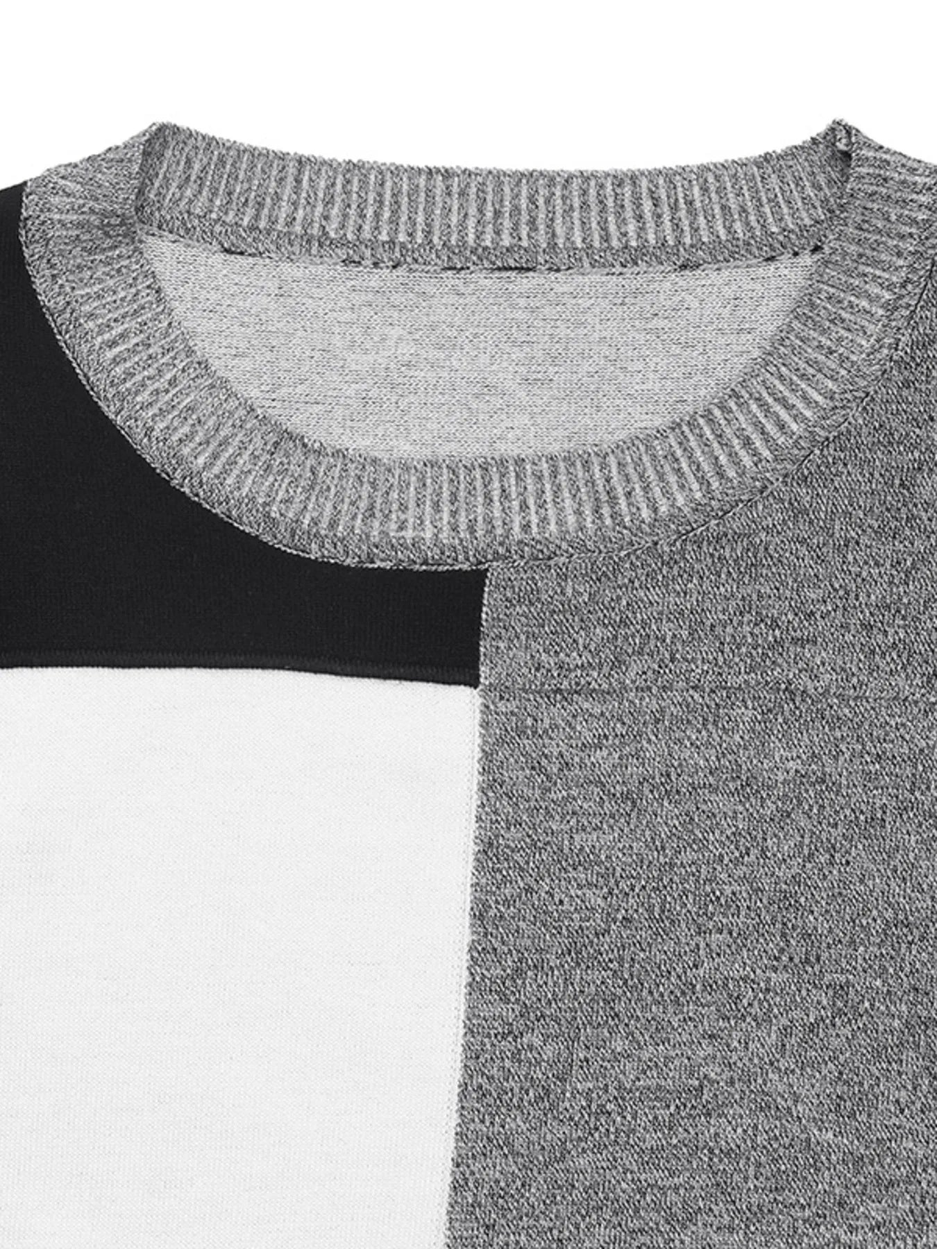 Close-up of a color block sweater with a ribbed crew neck and sections of black, white, and speckled gray fabric.