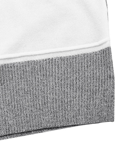 Close-up of a color block sweater with a ribbed crew neck and sections of black, white, and speckled gray fabric, super closed up.