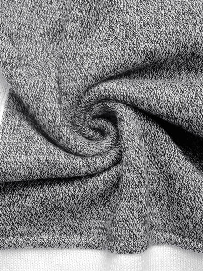 Close-up of a color block sweater with a ribbed crew neck and sections of black, white, and speckled gray fabric, twisted fabric.