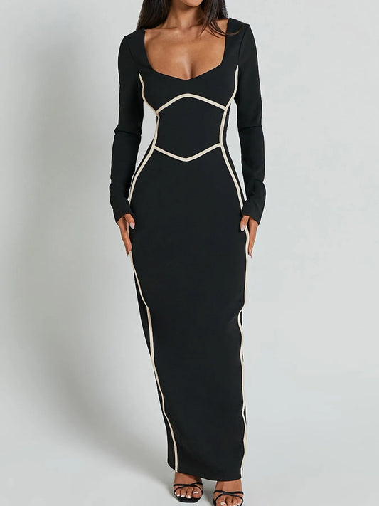 A full length form black dress with long sleeves and white trim details and has a geometric white pattern around the waist and shoulders.
