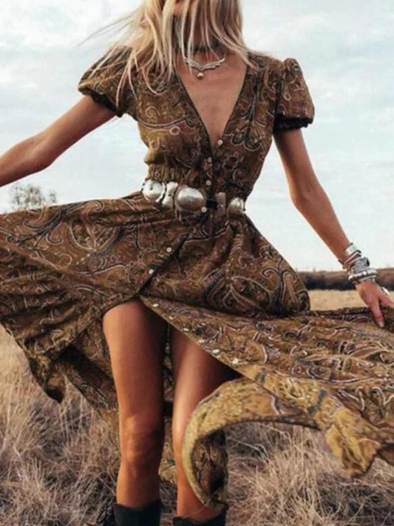 Woman wearing a flowing paisley print dress with puff sleeves, deep V-neckline, and high slit
