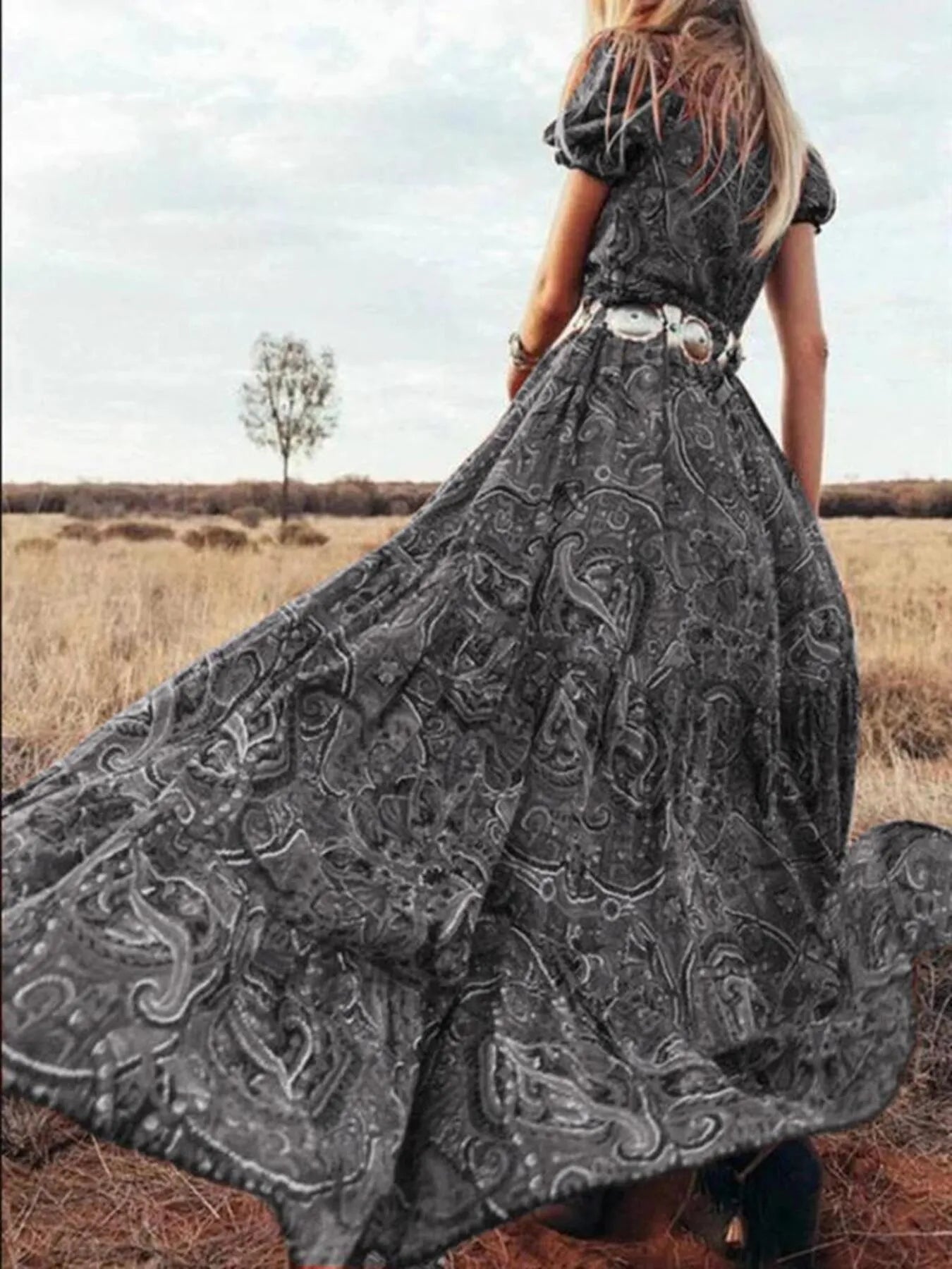 Woman wearing a flowing paisley print dress with puff sleeves, deep V-neckline, and high slit
