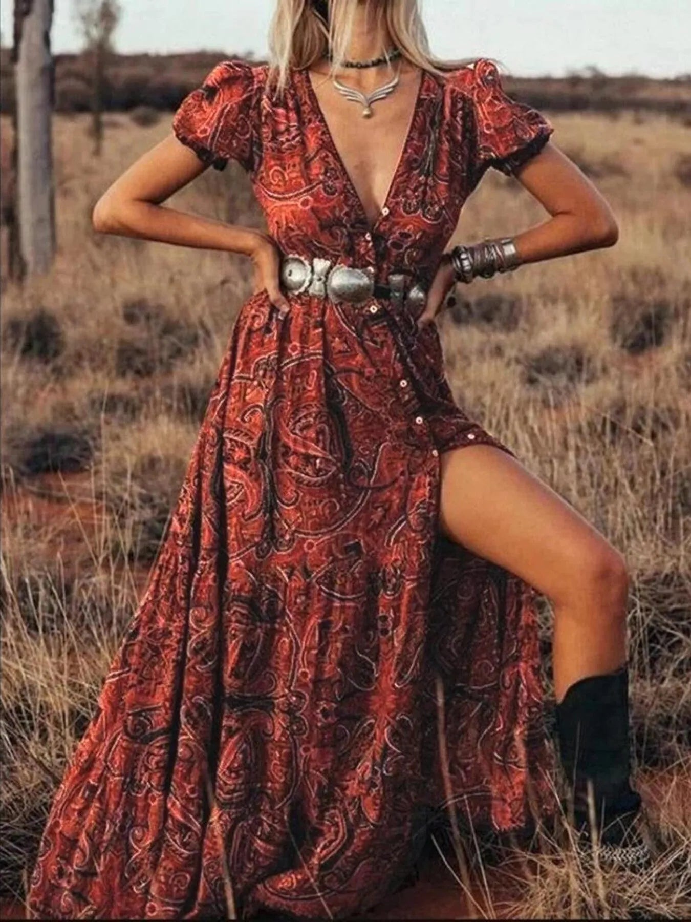 Woman wearing a flowing paisley print dress with puff sleeves, deep V-neckline, and high slit
