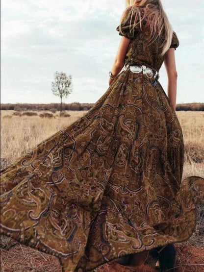 Woman wearing a flowing paisley print dress with puff sleeves, deep V-neckline, and high slit
