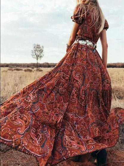 Woman wearing a flowing paisley print dress with puff sleeves, deep V-neckline, and high slit
