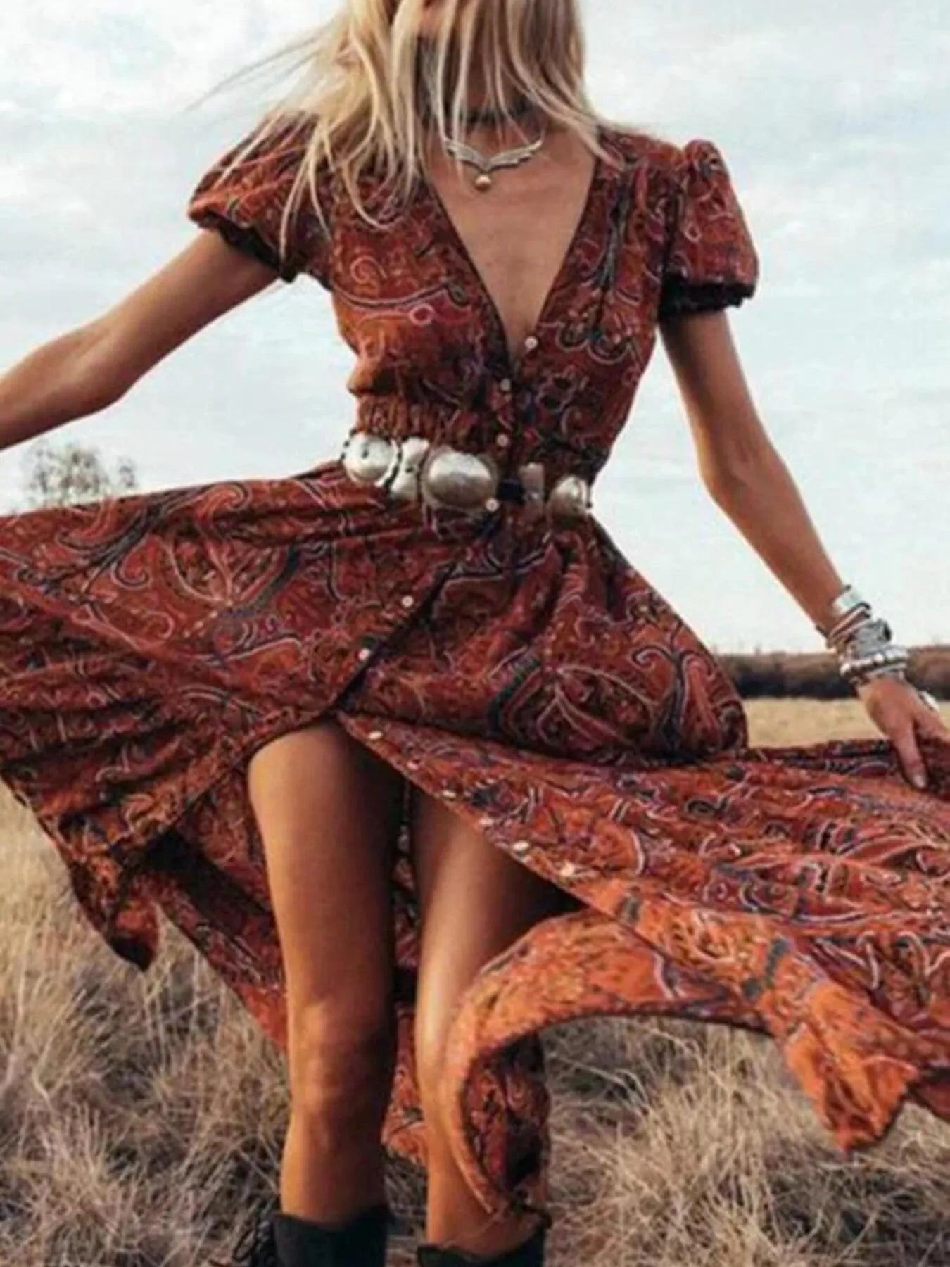 Woman wearing a flowing paisley print dress with puff sleeves, deep V-neckline, and high slit
