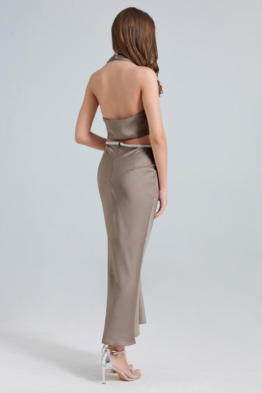 A sleek, taupe maxi dress with a twisted front knot and cut-out detail at the waist, fitted silhouette and a subtle high slit.