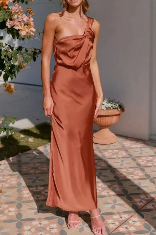A satin, terracotta-toned, one-shoulder gown with a wrapped bodice and a floor-length, sleek silhouette.