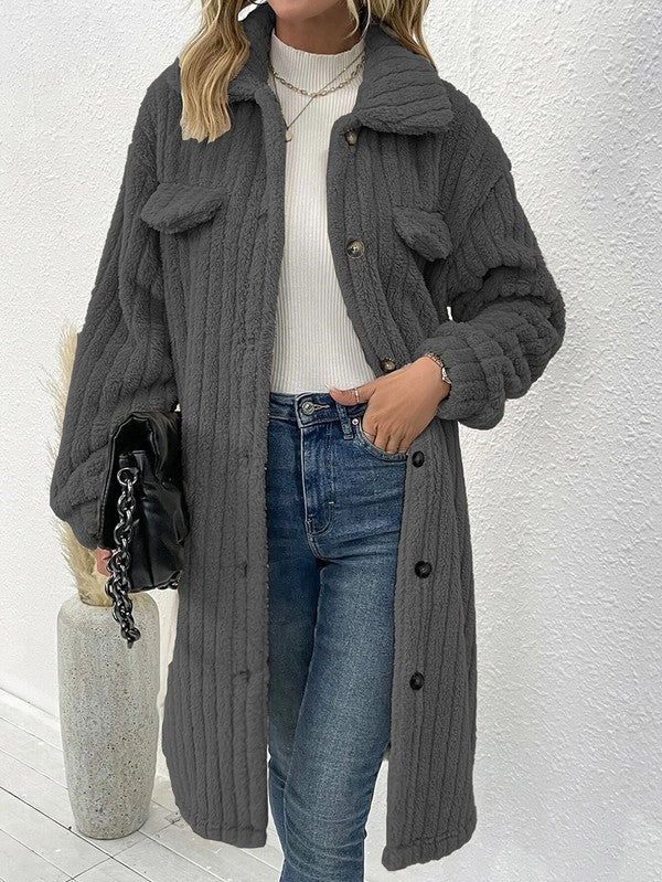 Person wearing a long gray coat with a white wall background
