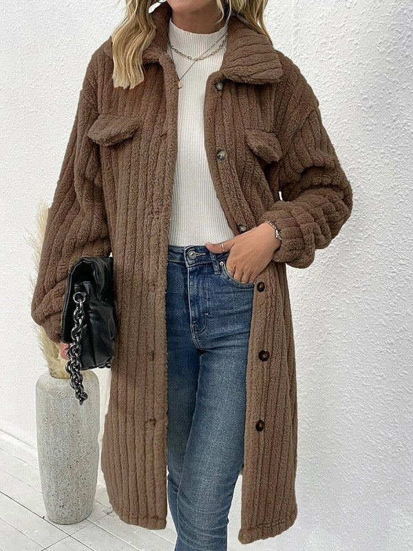 Person wearing a brown knitted coat with a white wall background