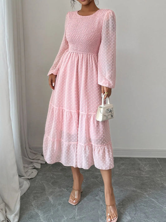 A pink dress features a fitted bodice with long sheer sleeves and a tiered flowing skirt that falls tomid-calf.