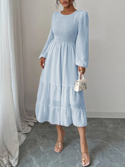 A  Light pastel blue features a fitted bodice with long sheer sleeves and a tiered flowing skirt that falls tomid-calf.