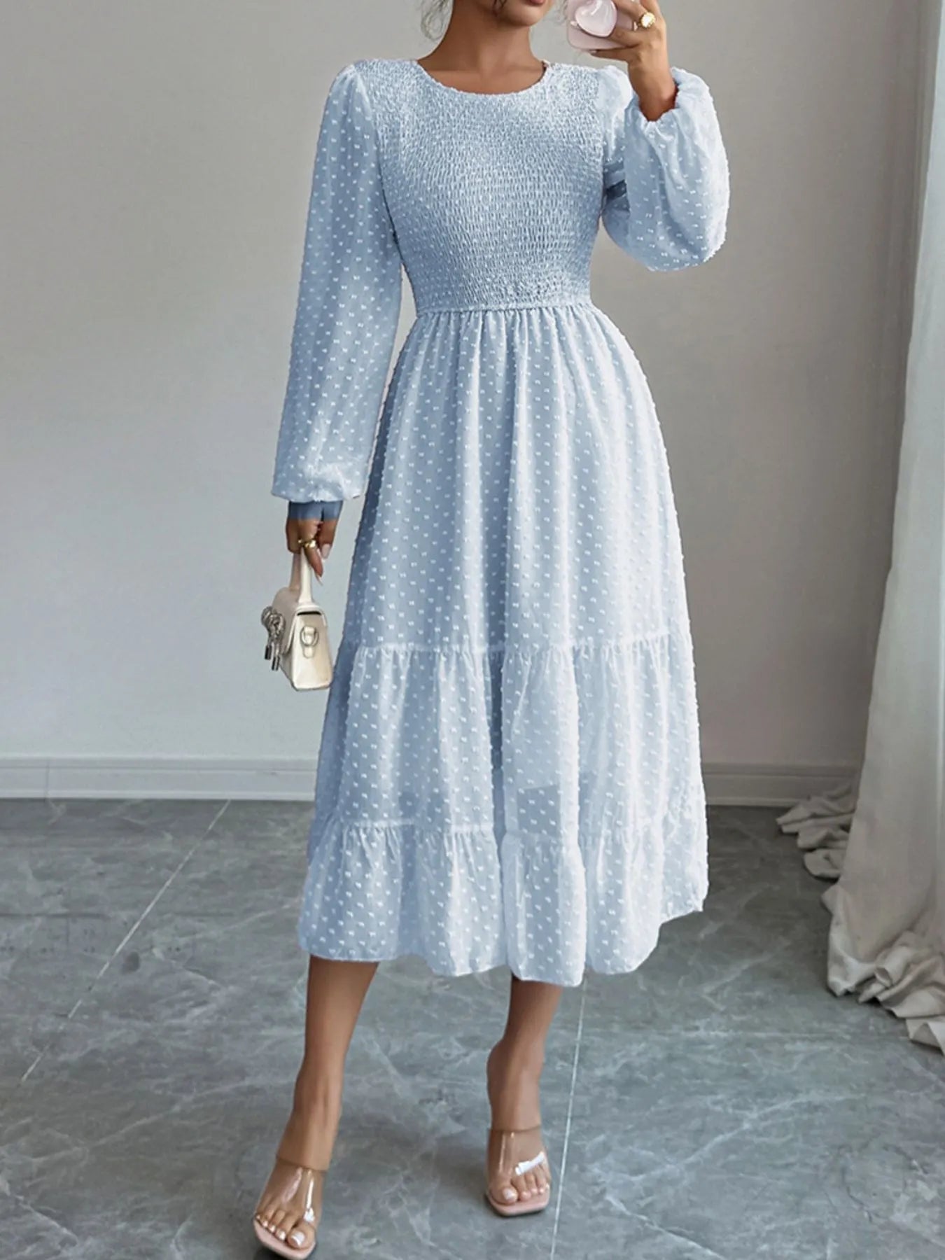 A  Light pastel blue features a fitted bodice with long sheer sleeves and a tiered flowing skirt that falls tomid-calf.