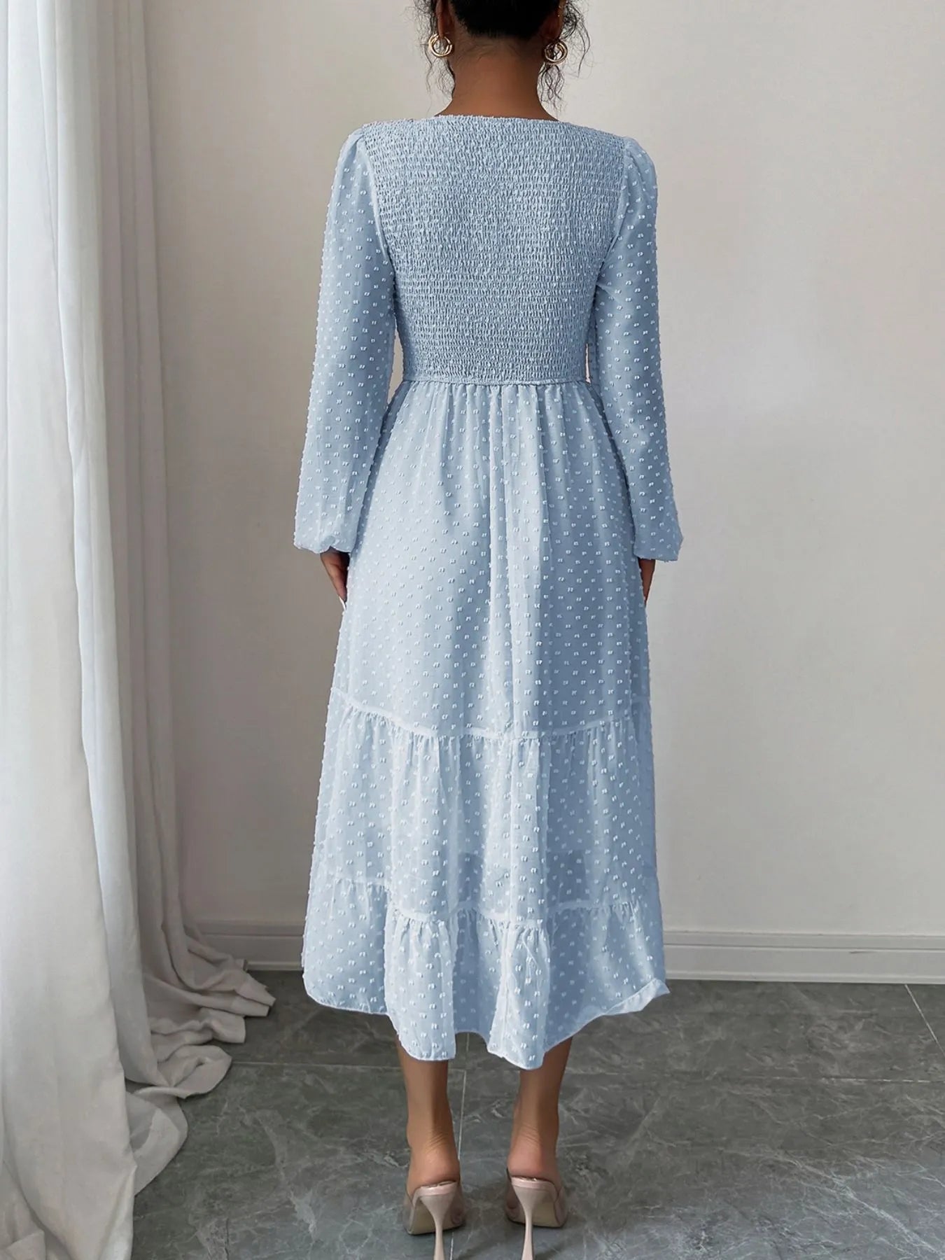 A  Light pastel blue features a fitted bodice with long sheer sleeves and a tiered flowing skirt that falls tomid-calf.