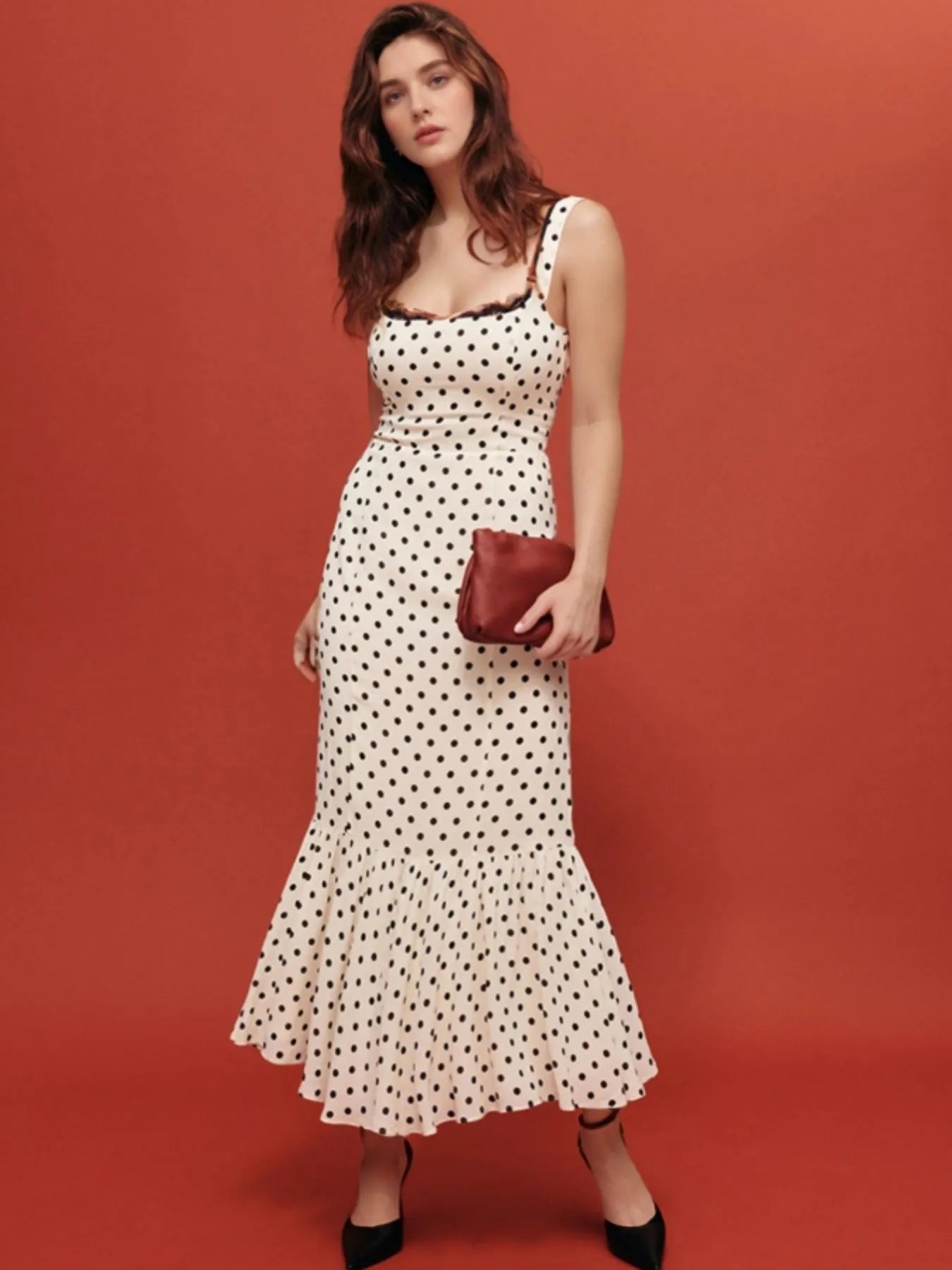 A white, polka-dotted, sleeveless maxi with a fitted bodice and a flared, ruffled hem that reaches the ankles.