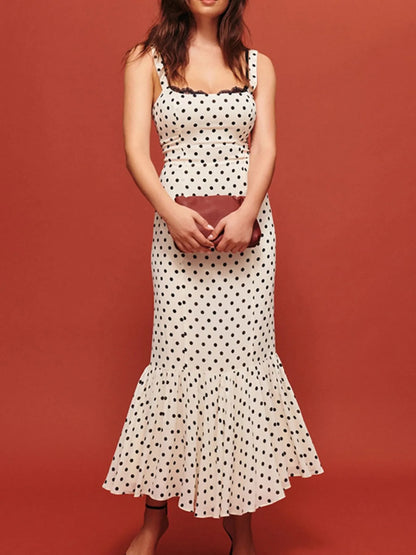 A white, polka-dotted, sleeveless maxi with a fitted bodice and a flared, ruffled hem that reaches the ankles.