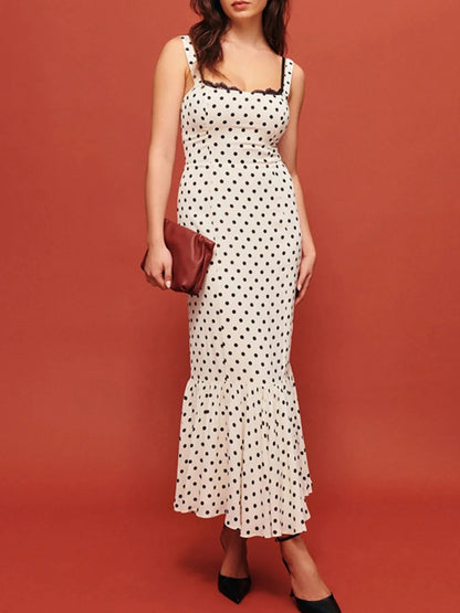 A white, polka-dotted, sleeveless maxi with a fitted bodice and a flared, ruffled hem that reaches the ankles.
