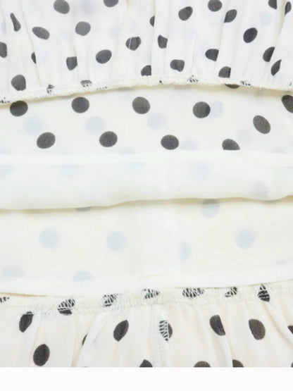 A white, polka-dotted, sleeveless maxi with a fitted bodice and a flared, ruffled hem that reaches the ankles