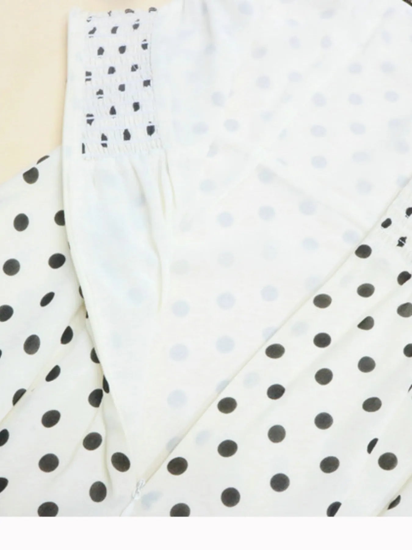 A white, polka-dotted, sleeveless maxi with a fitted bodice and a flared, ruffled hem that reaches the ankles